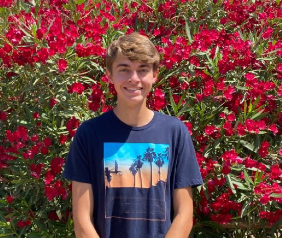 This image is a photo of Dylan Walters standing infront of a wall of red flowers.